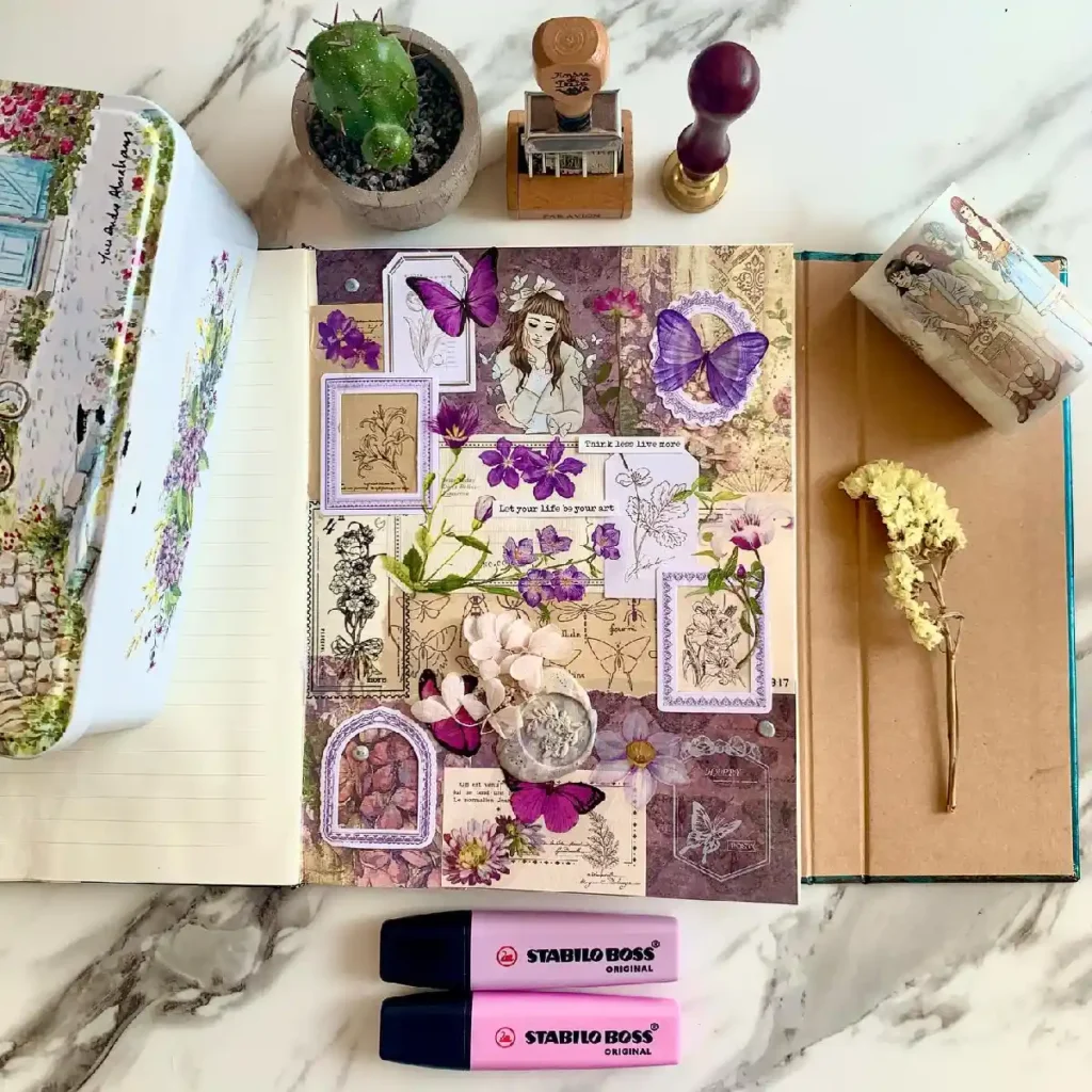 Artistic flat lay of a colorful journal with floral collages, butterflies, and stationery on a marble surface.