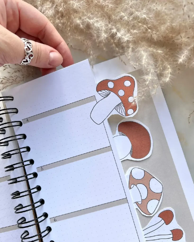 Close-up of a planner with mushroom stickers, featuring a hand turning the page and soft background textures.