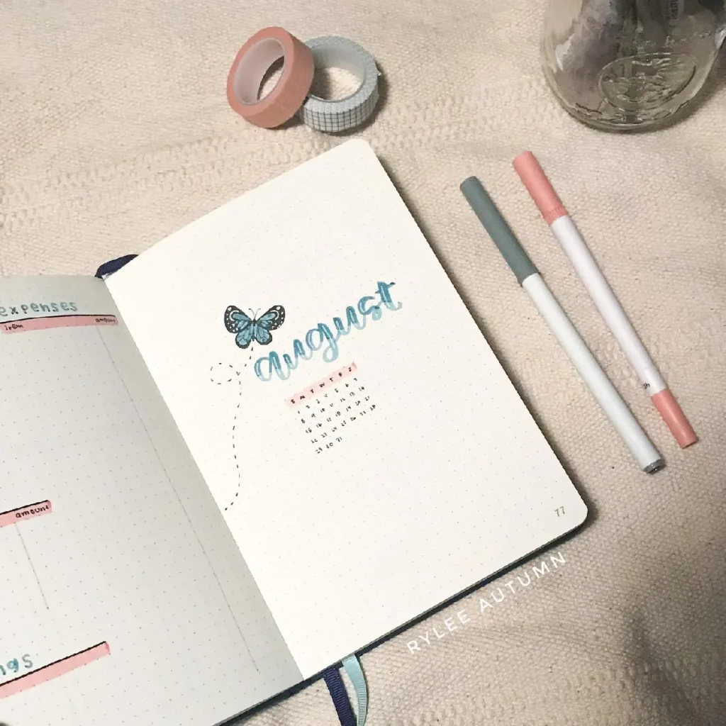 Bullet journal spread for August featuring a butterfly illustration, calendar, colorful pens, and decorative washi tape.