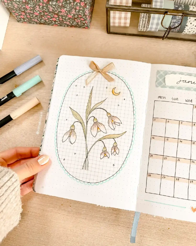 Hand-drawn floral illustration in a bullet journal, showcasing snowdrops and a decorative ribbon on dotted paper.